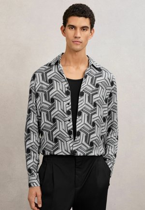 Mustvalge geomeetrilise mustriga pikkade varrukatega särk, avatud krae ja nööpidega, kombineeritud lihtsa musta pealse ja lõigatud mustade pükstega.