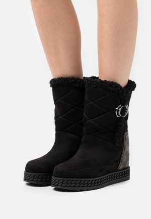 Black suede ankle boots with a quilted design, faux fur lining, and a decorative silver buckle; textured black rubber sole.