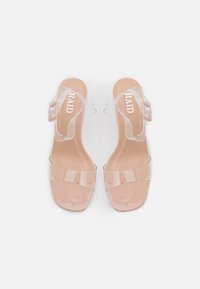 Paire de sandales à talons couleur nude avec brides en PVC transparent et boucle à la cheville, vues de dessus sur fond blanc.