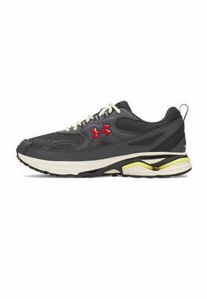 Zwarte en grijze sportsneakers met witte zool, gele accenten, witte veters en een rood logo aan de zijkant, zijaanzicht.