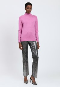 Engenehter rosa Rollkragenpullover mit gerippten Akzenten am Ausschnitt und an den Bündchen, kombiniert mit glänzenden silbernen gerade geschnittenen Hosen und spitzen schwarzen High Heels.