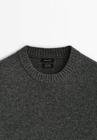 Pull gris foncé en maille avec col rond côtelé, montrant l'étiquette de la marque à l'intérieur de l'encolure sur fond blanc uni.