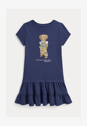 Κοντό φόρεμα σε μπλε ναυτικό χρώμα με βολάν στο τελείωμα και εικόνα αρκούδας που φοράει παντελόνια με μπαλώματα και γιλέκο πουλόβερ.