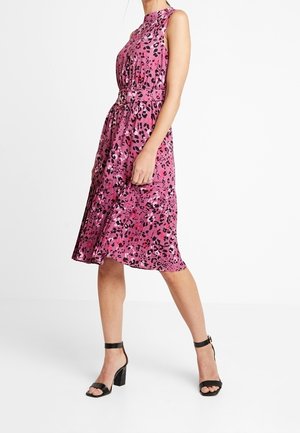 Vestido midi sin mangas con estampado de leopardo rosa y detalle de cinturón, combinado con sandalias negras de tacón ancho con correa al tobillo y punta abierta.