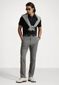 Svart polo-skjorte, grå genser lagt over skuldrene, grå dressbukser og hvite sko. Tilbehør inkluderer solbriller og et sølvbelte.