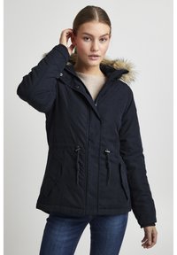 Navy blue parka jacket with a fur-trimmed hood, drawstring waist, and two front pockets. Smooth texture and zip closure.