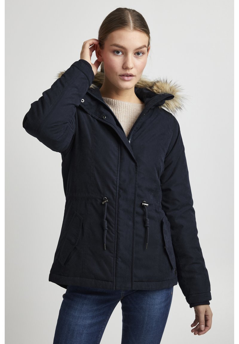 Parka bleu marine avec capuche en fourrure, taille à cordon de serrage et deux poches avant. Texture lisse et fermeture éclair.