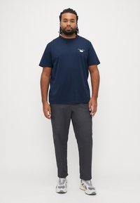 Tamsiai mėlynas medvilninis marškinėlis trumpomis rankovėmis, su mažu piešiniu kairiajame krūtinės plote; derinamas su pilkomis kelnėmis ir baltomis sportinėmis bateliais.