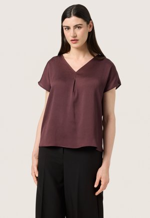 Bordeaux kortærmet bluse med V-hals, plissering foran, afslappet pasform og blødt, tekstureret stof. Kombineret med sorte bukser.