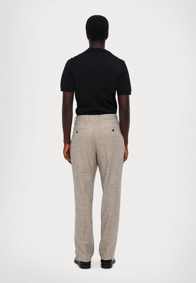 Zwarte T-shirt met korte mouwen gecombineerd met lichtbeige broek met ruitpatroon. De broek heeft achterzakken en een rechtmodel. Zwarte schoenen zijn zichtbaar.