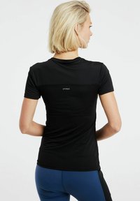 Čierne športové tričko s priliehavým strihom, hladkou textúrou a horizontálnymi pruhmi na hornom chrbte. Logo zobrazené na zadnej strane.