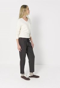 Krémový svetr s výstřihem do V, tmavě šedé jogger kalhoty s šňůrkou a hnědé tenisky s bílými tkaničkami. Měkká, pohodlná látka se bočními pruhy.