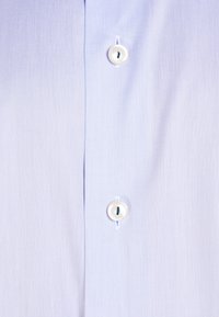 Světle modrá košile s hladkou texturou, s bílými knoflíky a jemnými diagonálními pruhy na látce. Klasický límec.