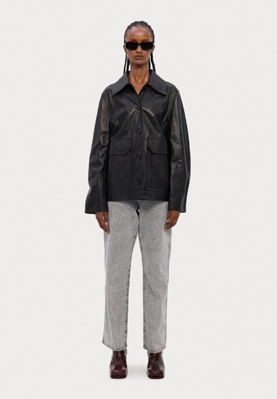 Must tumesnahkjack, millel on kraega kaelus, esine nupud ja kaks suurt taskut, kombineeritud heledate hallide teksade ja tumepruunide saapadega.