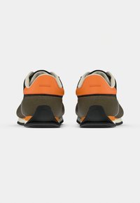 Sneaker mit zweifarbiger Optik, braunem Wildleder im unteren Bereich, schwarzem Obermaterial und leuchtend orangefarbenen Akzenten. Abgerundete Form mit strukturiertem Fersenbereich und gepolstertem Schaft.