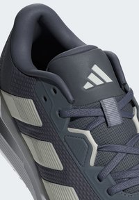 Gray athletic shoe with textured upper, padded collar, and contrasting light gray accents. Features signature logo and textile laces.