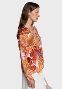 Blouse à manches longues multicolore avec un motif paisley en tons orange, rouge, jaune et violet, dotée d'un col rond et d'une coupe ample.