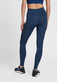 Marine blauwe leggings met een textuurpatroon langs de zijnaden, een hoge tailleband en een strakke pasvorm, gecombineerd met zwarte sportschoenen.