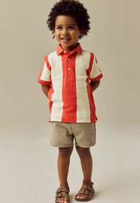 Rød og creme stribet polo shirt med en tekstureret finish, parret med beige shorts og brune sandaler. Kortærmet og med kravedesign.