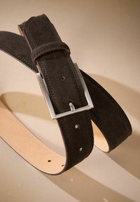 Sötétbarna velúr öv ezüst négyzet alakú csattal. Varrott részletekkel és több lyukkal a beállításhoz. Simító bőr alsó résszel.