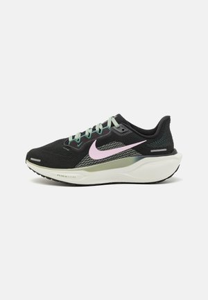 Zapatilla deportiva negra con parte superior de malla, cordones verde menta, un logo en forma de swoosh rosa y una suela blanca acolchada. Presenta un panel en el talón texturizado.