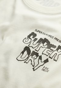 Witte katoenen t-shirt met grote zwarte grafische tekst "SUPER DRY" met een druip-effect, en kleinere tekst erboven en eronder.