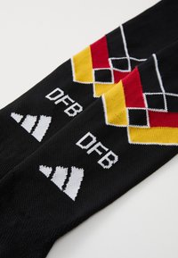 Meias desportivas pretas com padrão de losangos em vermelho, amarelo e branco, texto "DFB" e logótipo branco da Adidas sobre um fundo branco.