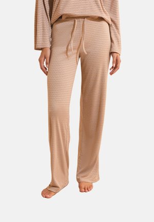 Persona con pantalones de descanso beige con rayas y cintura con cordón, combinados con parte superior de manga larga a juego, de pie descalza.