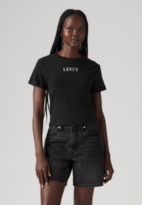 Schwarzes kurzärmliges T-Shirt mit Levi's-Logo, kombiniert mit hoch taillierten schwarzen Denim-Shorts. Glattes Material und lockere Passform.