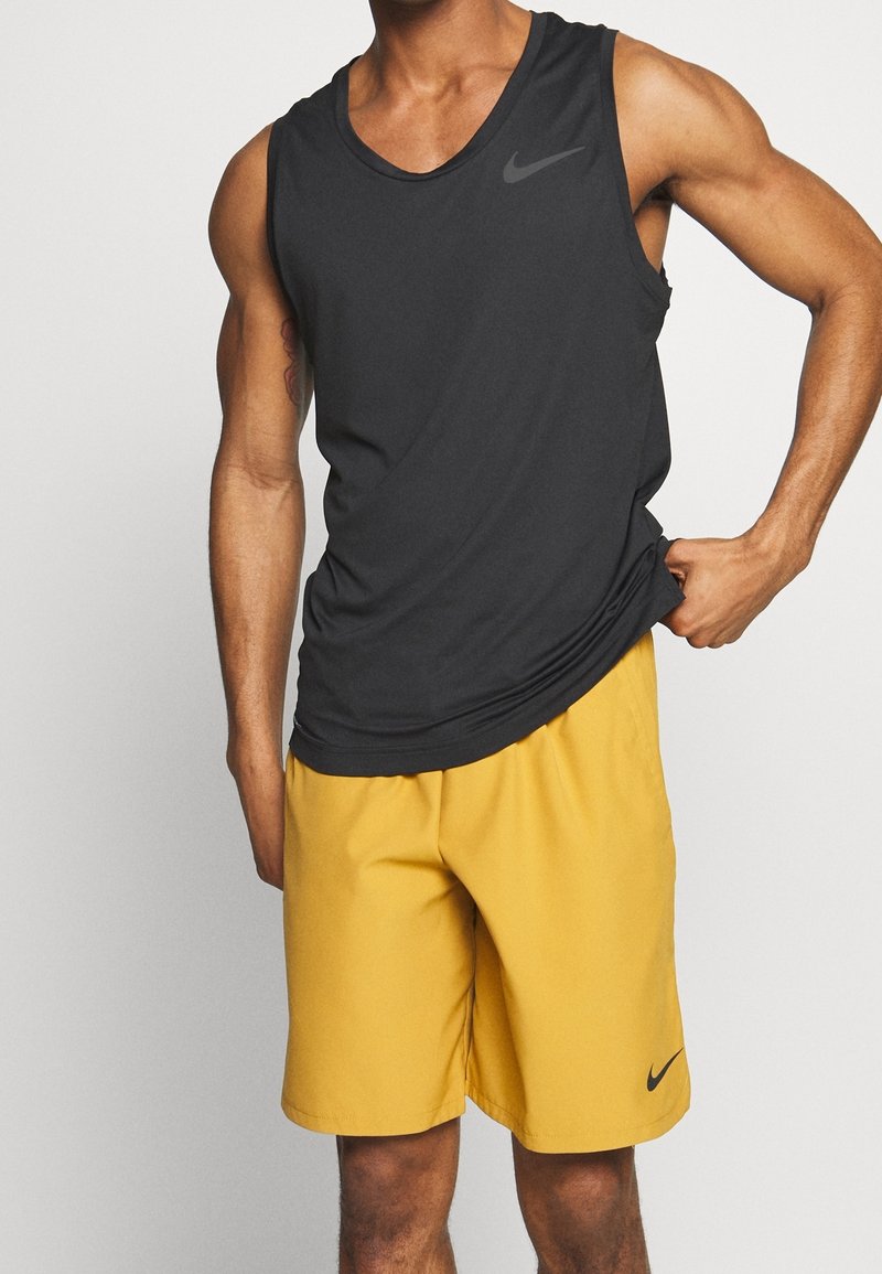 Haut sans manches gris foncé Nike avec encolure ronde, associé à un short de sport jaune. Logo noir sur le haut et le short. Tissu lisse, coupe décontractée.