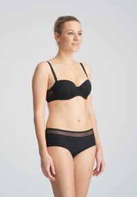 Czarny zestaw bielizny z usztywnianym, wyściełanym biustonoszem typu balkonette oraz dopasowanymi majtkami hipster. Biustonosz ma cienkie ramiączka i przezroczyste akcenty.