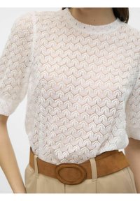 Blusa blanca texturizada con un patrón geométrico, que cuenta con mangas abullonadas cortas y escote redondo. Cinturón de gamuza beige delgado con una hebilla circular.