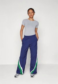 Siva oprijeta majica in modre športne hlače s stranmi zelenih in belih črt, ki nudijo udobno prileganje in žepke, kombinirane s sivimi supergami.