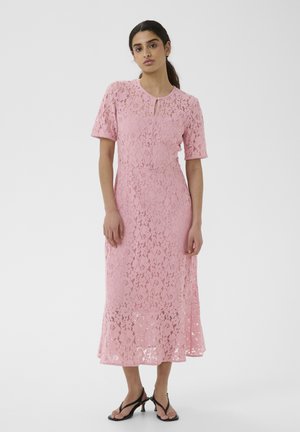 Tumejuustega naine madala hobusesabaga, kes kannab keskmise pikkusega roosat pitskleiti lühikeste varrukatega ja musti kontsakingi.