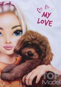 Maglietta grafica con una ragazza dai capelli biondi e occhi azzurri che tiene in braccio un cucciolo marrone. Il testo recita "IL MIO AMORE" in rosa glitterato, con cuori sopra.