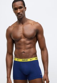 Tmavomodré boxerky s žltým pásom a logom Nike. Vyznačujú sa mäkkou látkou a priliehavým dizajnom pre pohodlie a oporu.