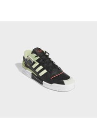 Svart och grön sneaker med övre av mocka och läder, vit mellansula, svart yttersula och tre vita ränder på sidan.