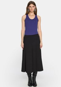 Fioletowy top bez rękawów połączony z czarną, dług ą spódnicą, o gładkiej teksturze i subtelnymi fałdami; czarne kozaki do kolan dopełniają całość.