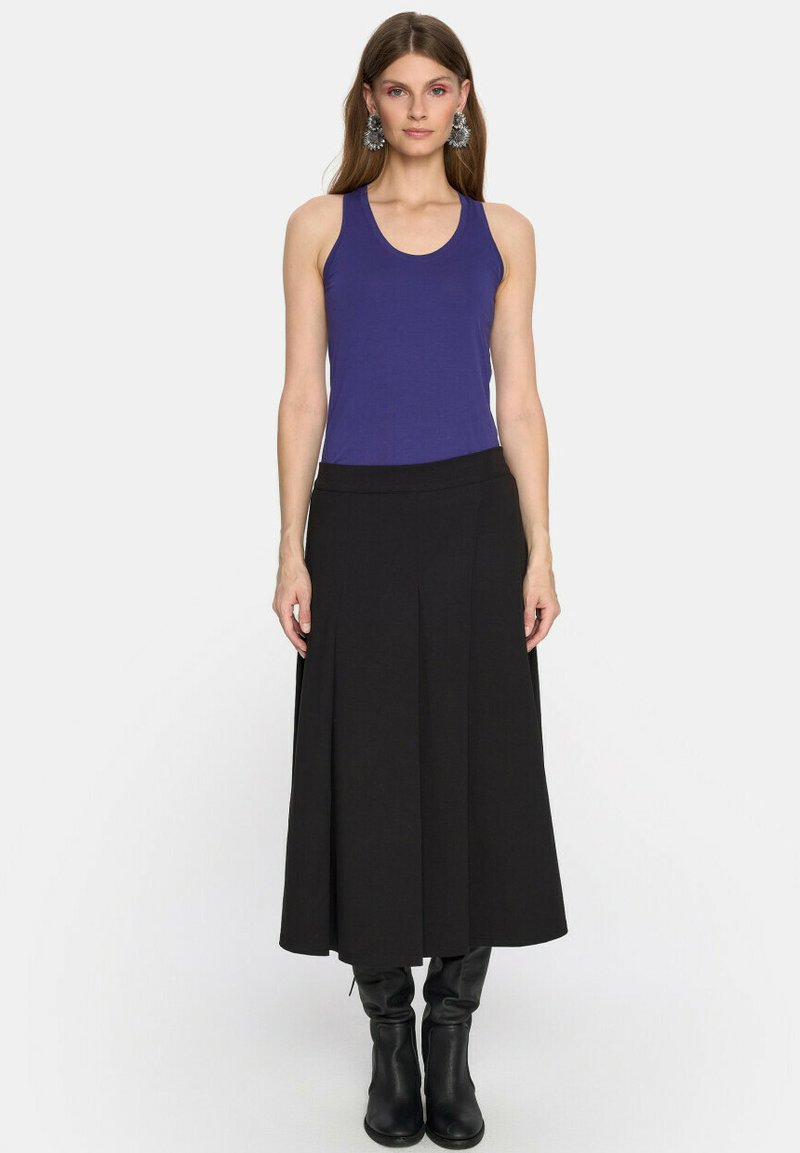 Fioletowy top bez rękawów połączony z czarną, długą spódnicą, o gładkiej teksturze i subtelnymi fałdami; czarne kozaki do kolan dopełniają całość.