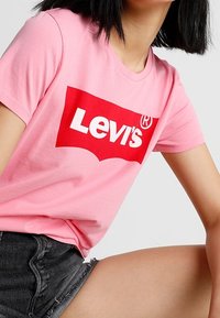 Růžové bavlněné tričko s bílým logem "Levi's" na červeném pozadí. Krátké rukávy a klasický kulatý výstřih.