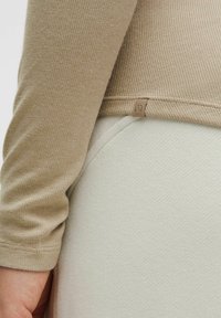 Maglietta a maniche lunghe con una texture ribbed beige, abbinata a un tessuto morbido verde chiaro. Presenta un piccolo marchio etichetta sull'orlo.