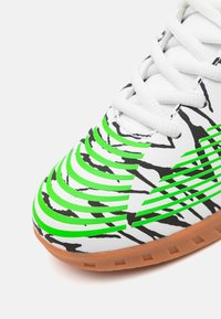 Sneakers z białą syntetyczną cholewką, zielonymi i czarnymi akcentami w falisty wzór, teksturowaną podeszwą i białymi sznurowadłami. Posiada gumową podeszwę.