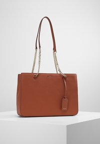 Sac fourre-tout en cuir marron avec des poignées plates doubles et des accents en chaîne. Il dispose d'une plaque logo et d'une étiquette amovible pour plus de détails.