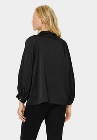 Black blouse with a smooth, lightweight fabric. Features long, balloon sleeves and button details at the cuffs. Loose, draped design.