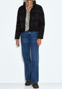 Svart puffjacka med hög krage, matchad med en ljusgrå tröja, blå jeans och gröna skor. Slät textur, kort design.