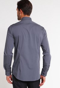 Camicia grigia a maniche lunghe con colletto strutturato, texture liscia e polsini abbottonati. Ha una vestibilità su misura e un design con yoke posteriore.