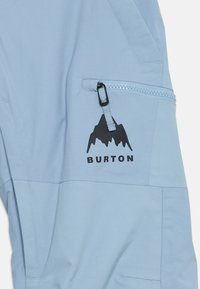 Ανοιχτό μπλε παντελόνι χιονιού από ύφασμα με φερμουάρ και μαύρο λογότυπο βουνού με κείμενο "BURTON" από κάτω. Λείος υφασμάτινος τύπος, ελαφρύ σχέδιο.