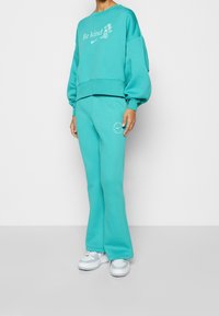 Turquoise sweatshirt with "Be kind" text and a floral design, paired with matching flared sweatpants featuring logo accents and cuffs.