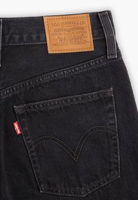 Poche arrière d’un jean noir Levi’s avec couture arcuate signature, étiquette rouge Levi’s et étiquette de marque en cuir fauve à la ceinture.