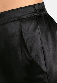 Pantalons en satin noir avec une texture lisse, dotés d'une taille élastique et de poches latérales. Le design offre une apparence élégante et cintrée.